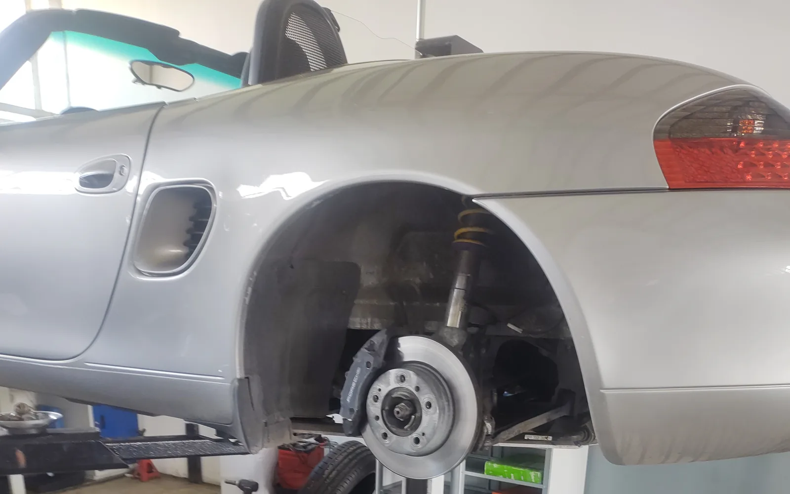 Сребристо Porsche Boxster на подемника със свалено колело и открито окачване